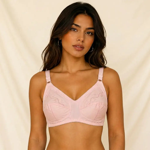 A woman modeling a light pink seamless bralette with scalloped lace detailing on the cups, set against a soft beige fabric backdrop.