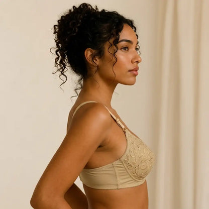 A woman in side profile wearing a beige lace-trimmed bra against a soft cream background.